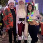 two people dressed in holiday outsite, posing wtih Santa